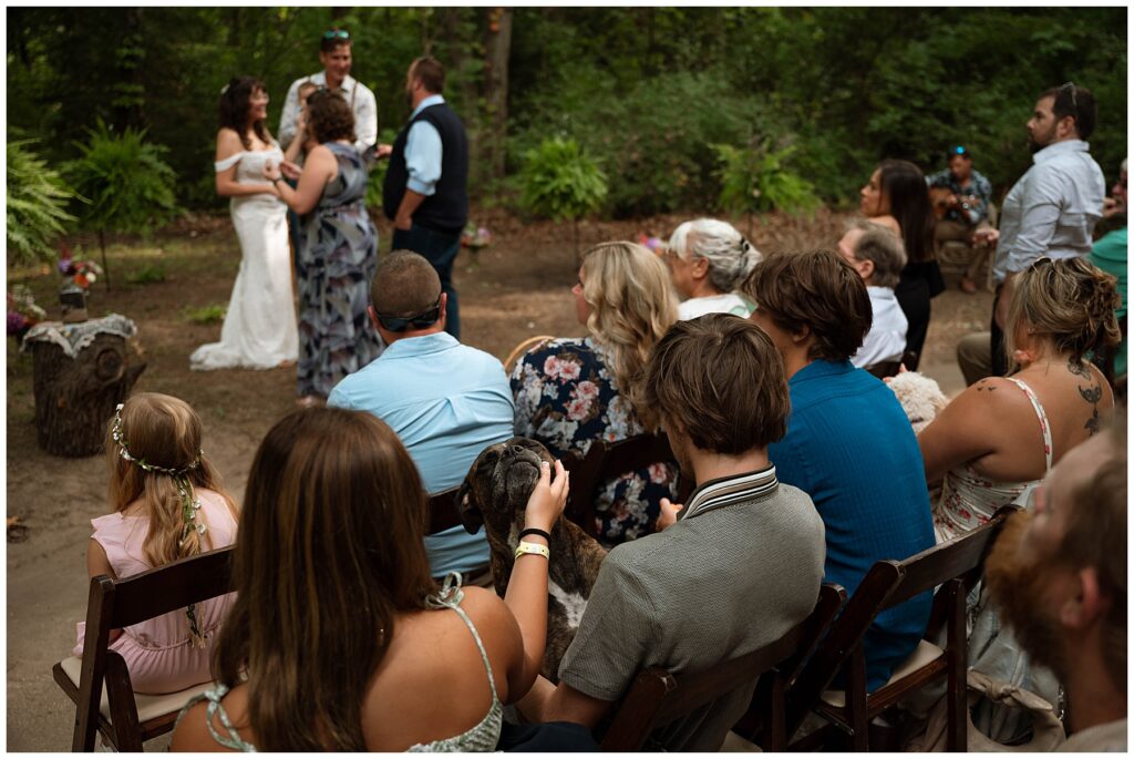 Dog enjoying love from wedding guest during outdoor wedding ceremony.