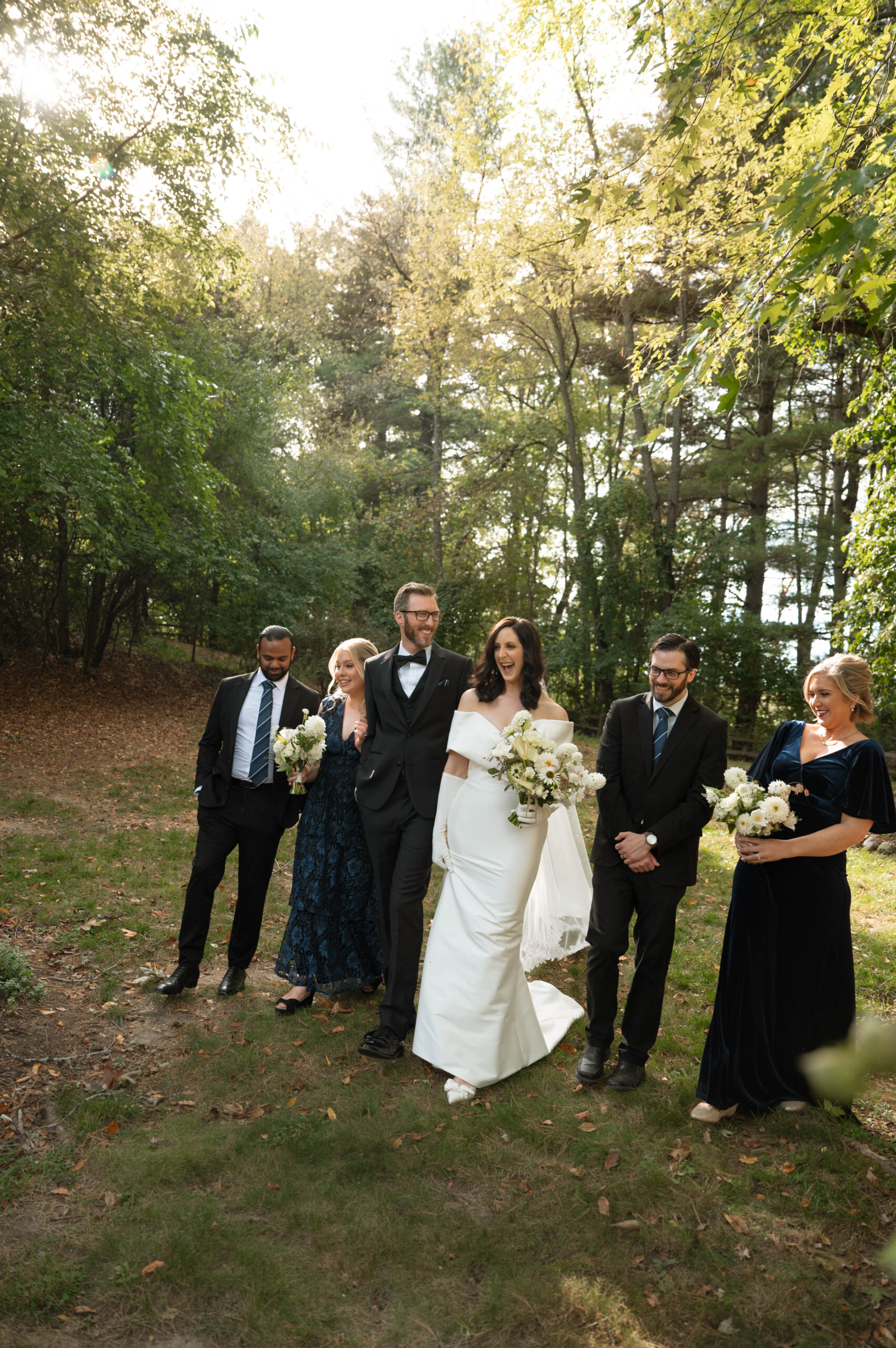 Wedding party walks with bride and groom surrounded by the greenery of Michigan.