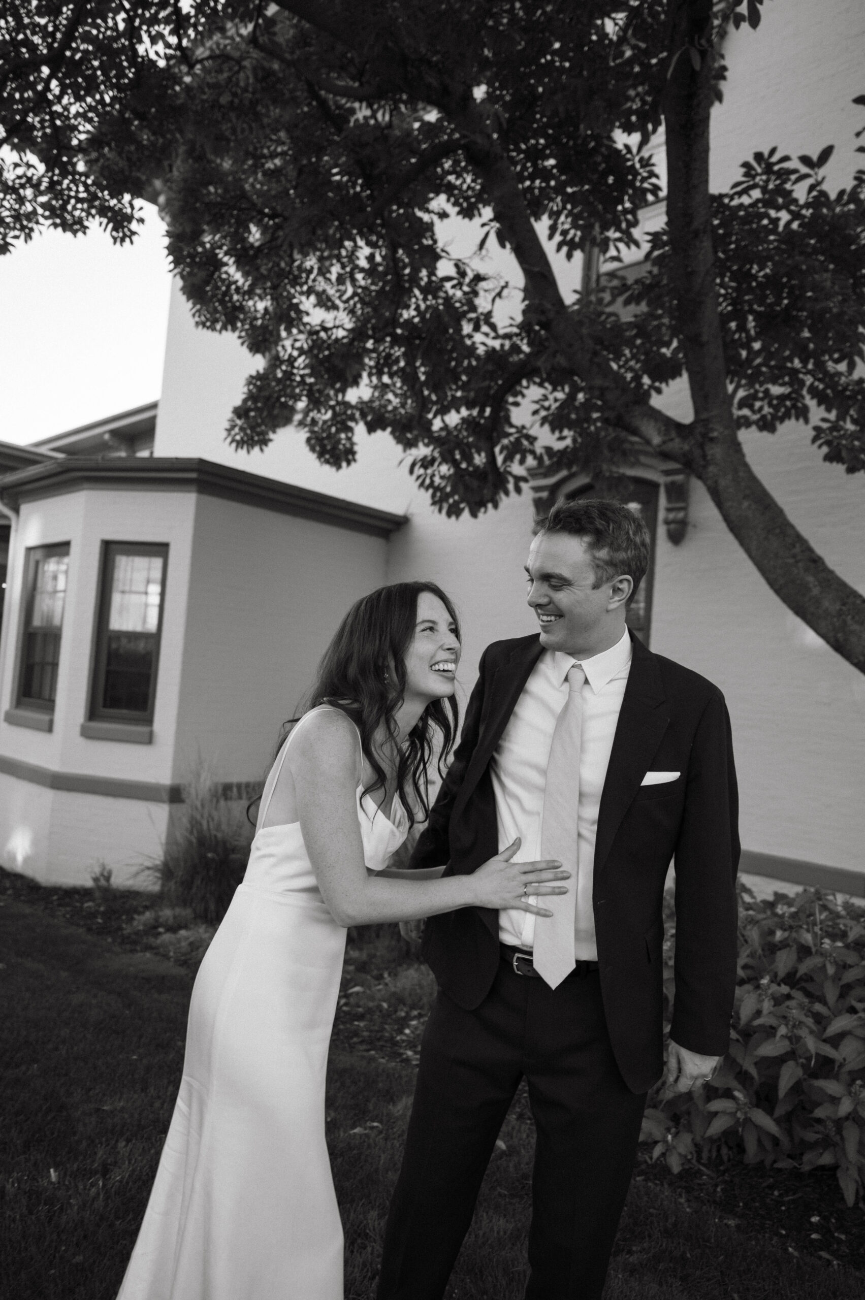 newlyweds laugh together outdoors next to their wedding venue